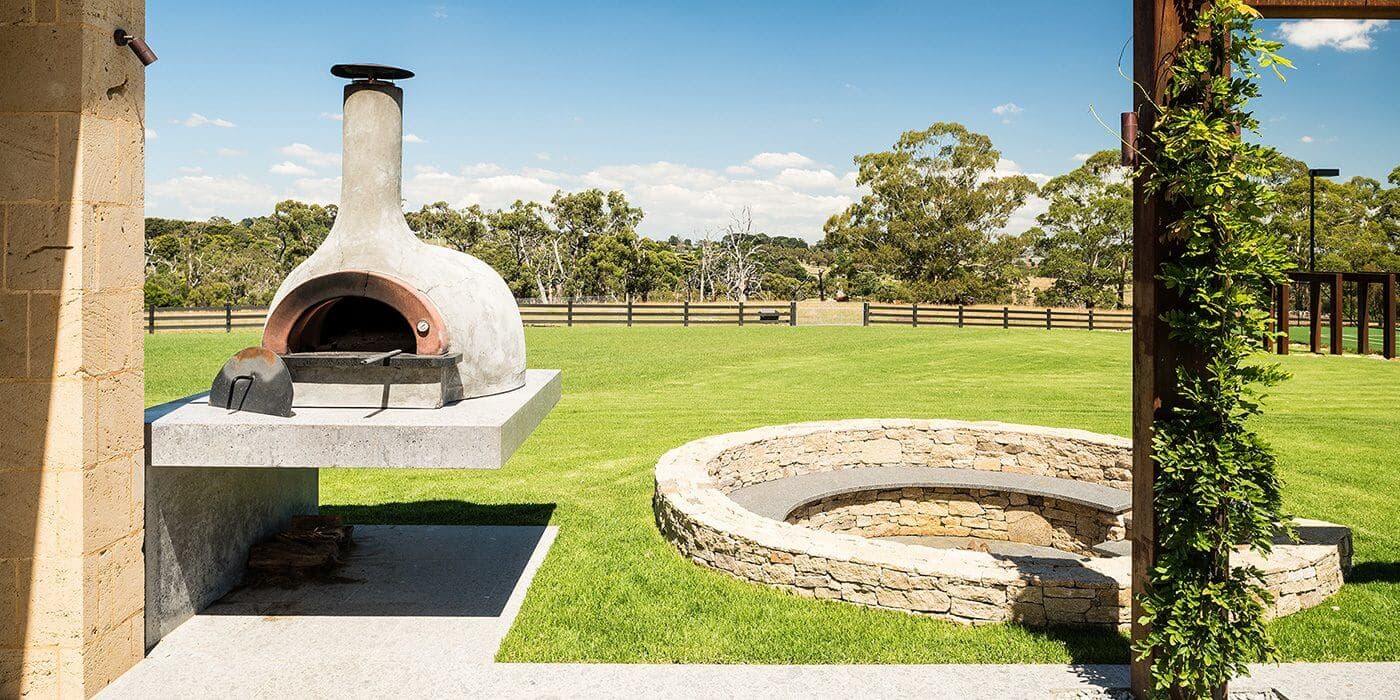 Outdoor wood fired pizza oven and circular stone fire pit in landscaped garden